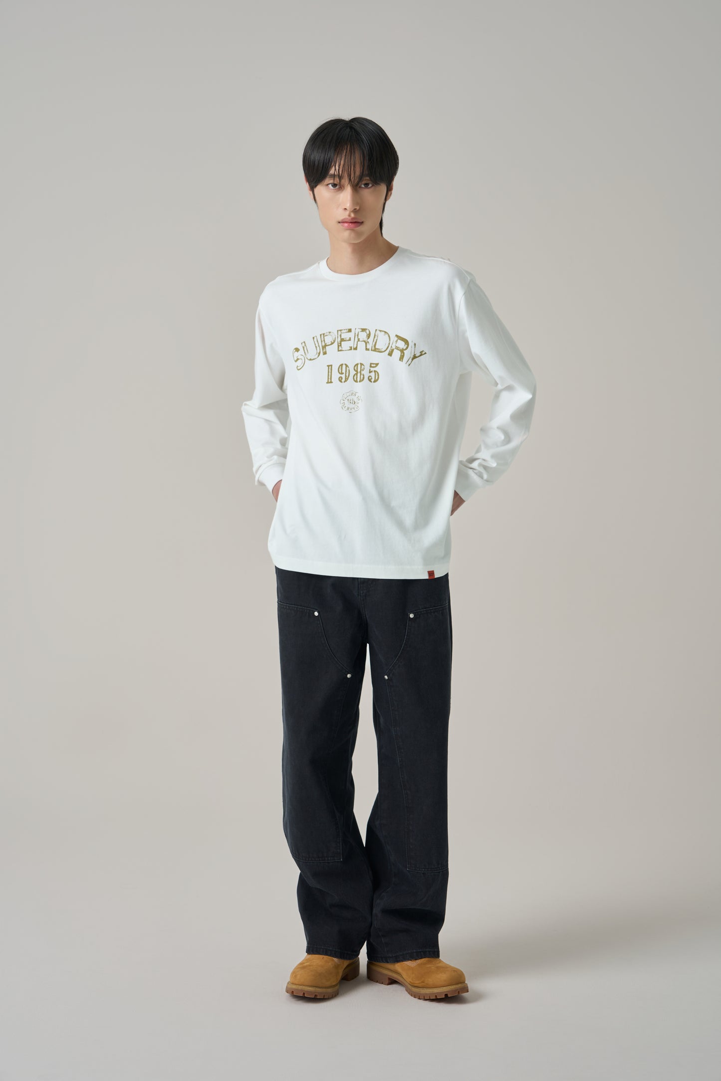 Person wearing a SuperDry white sweatshirt with text and dark pants on a plain background