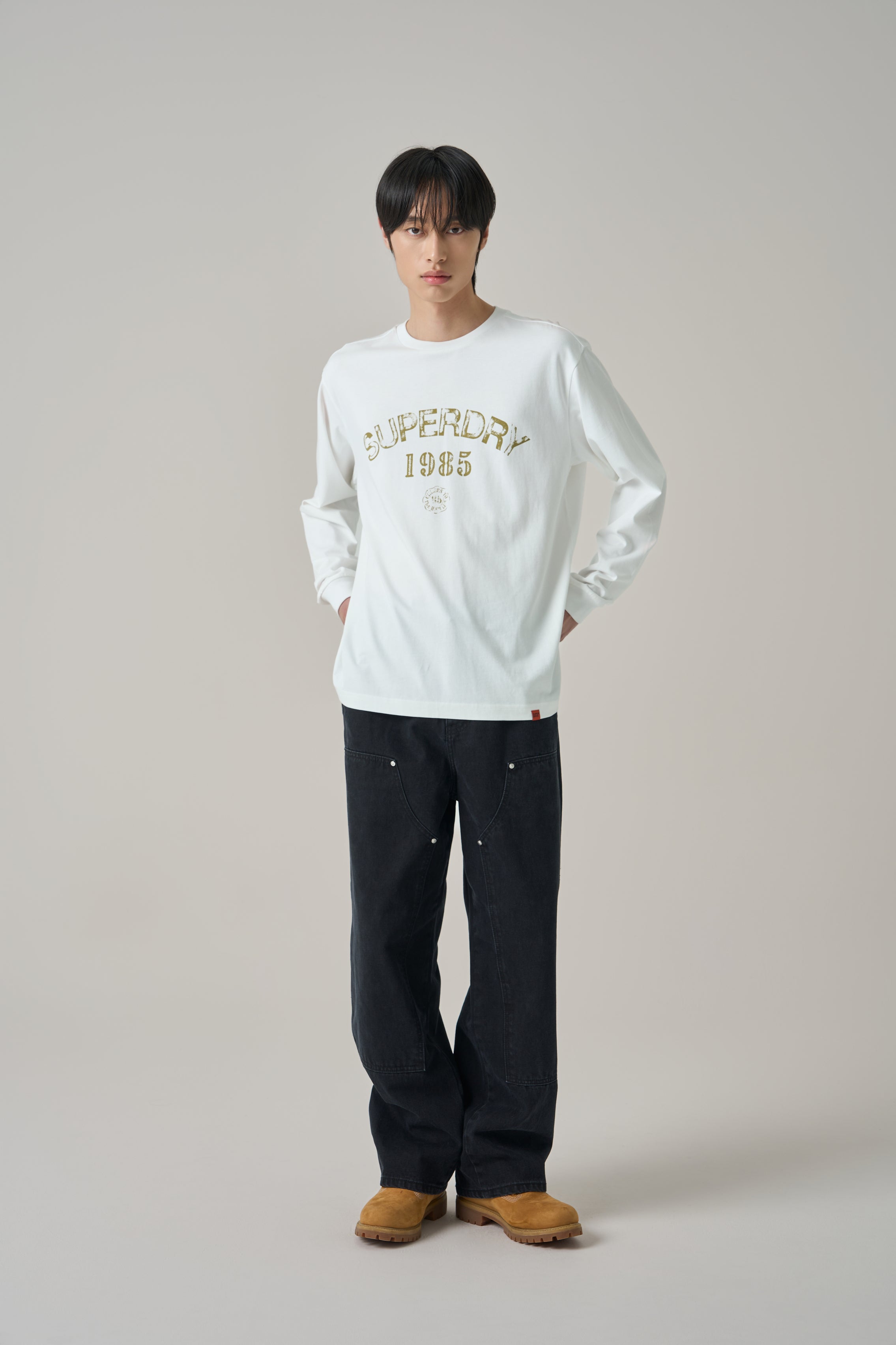 Person wearing a SuperDry white sweatshirt with text and dark pants on a plain background