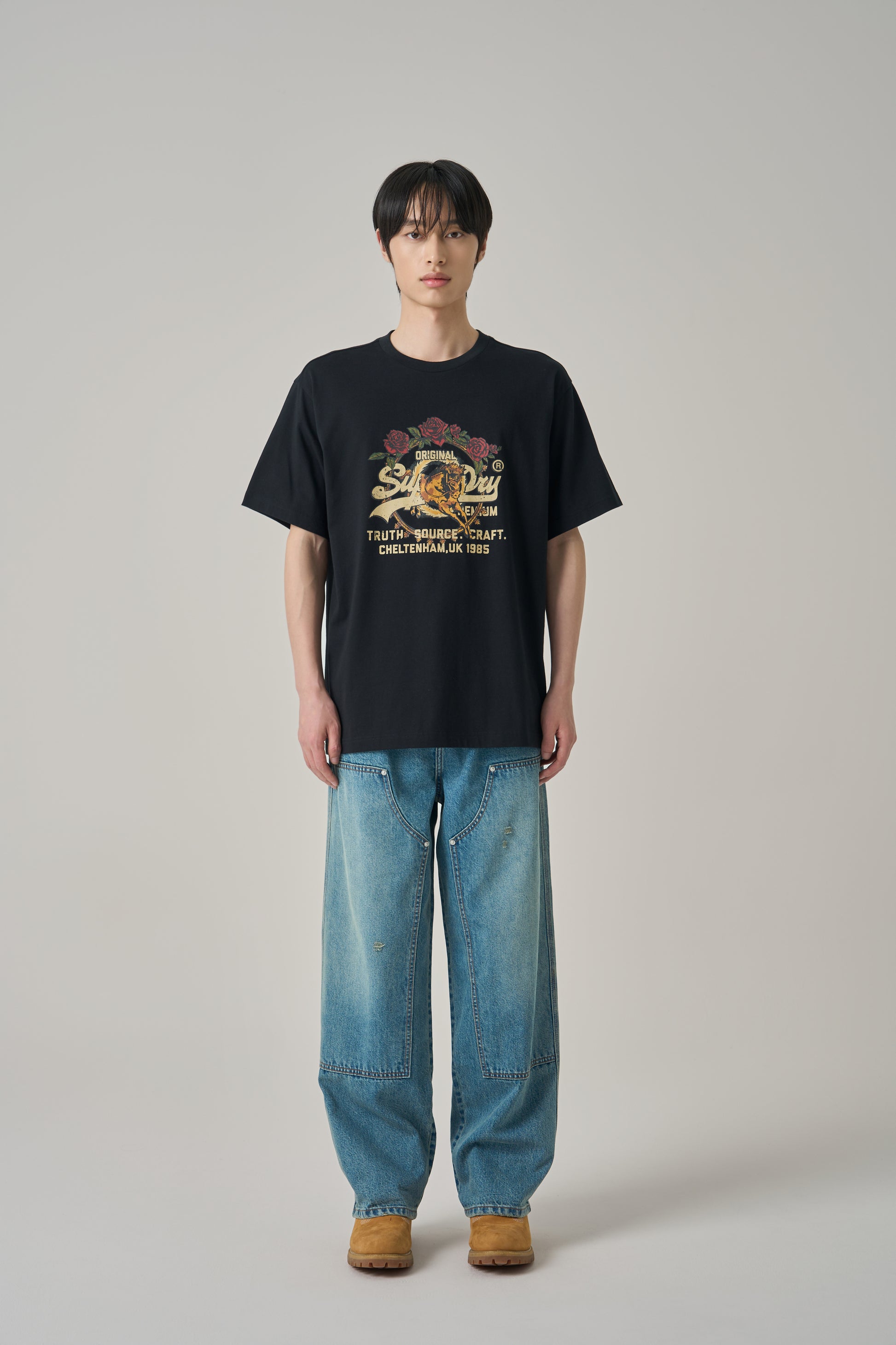 Person wearing a black t-shirt with a graphic design and blue jeans on a plain background