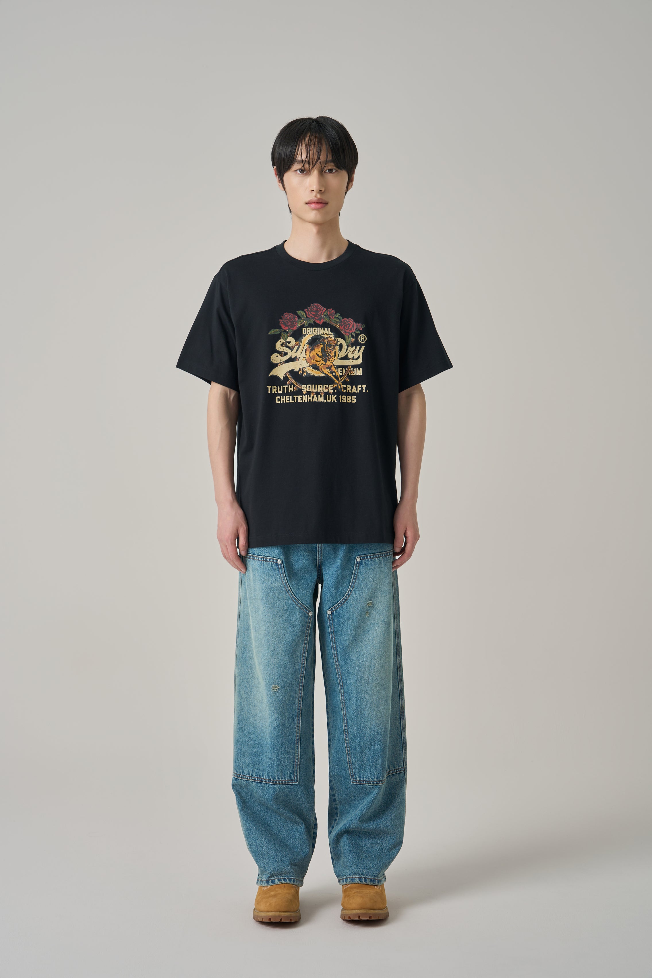 Person wearing a black t-shirt with a graphic design and blue jeans on a plain background