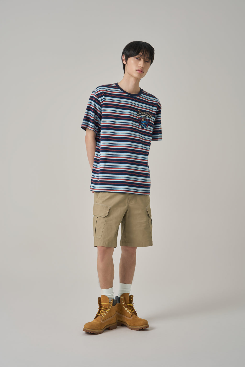 Person wearing a striped t-shirt, cargo shorts, and brown boots on a plain background